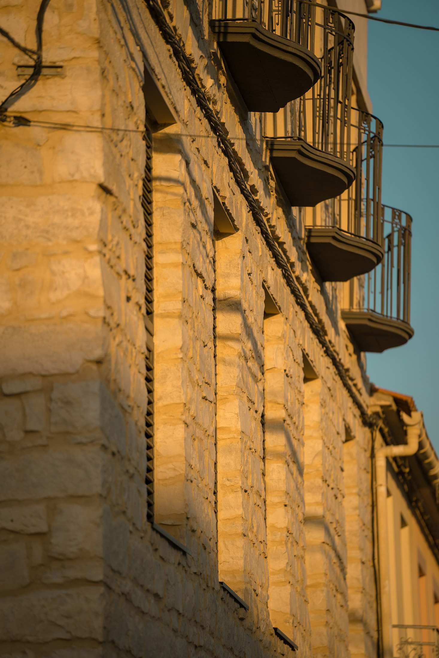Detalle arquitectónico de la fachada de piedra y un balcón metálico en la planta superior